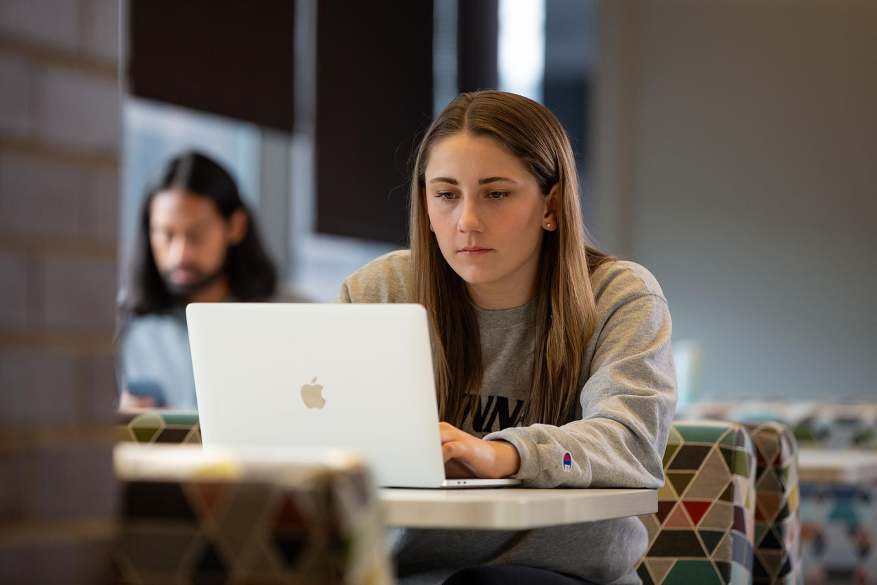 Young woman sitting at lop in study area with a view of a male student sitting nearby in the background