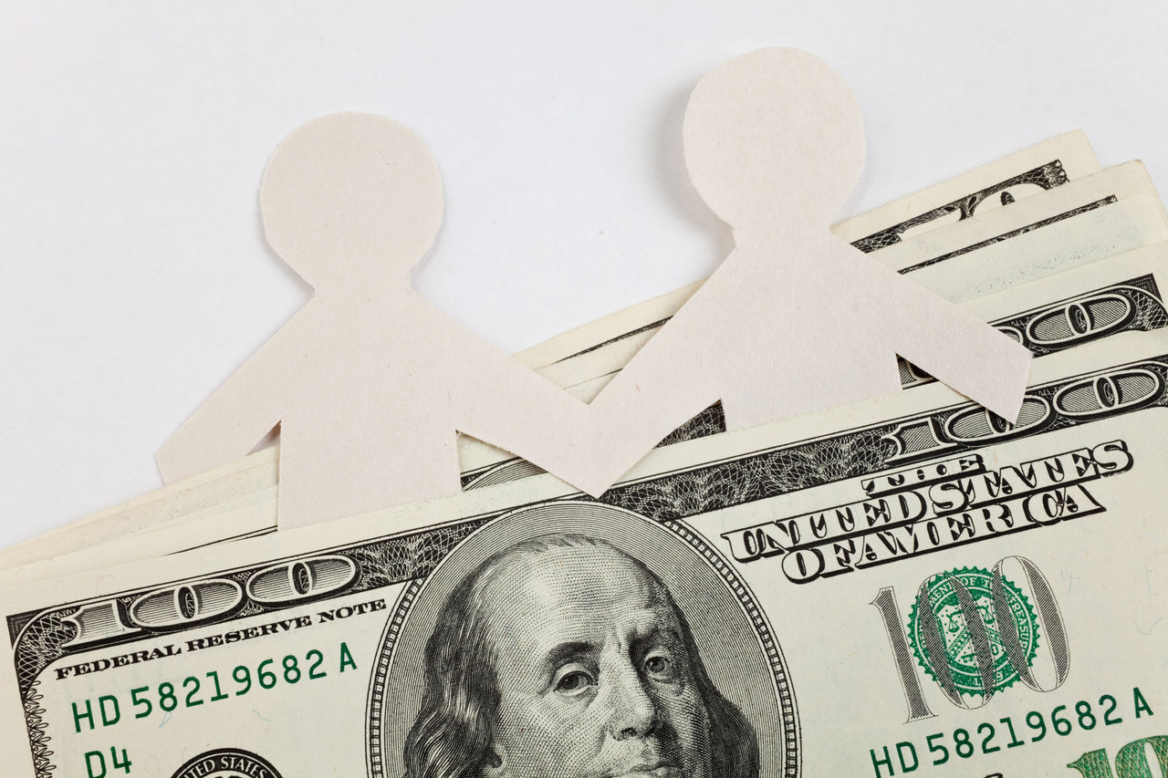 Two paper chain people nestled in a stack of cash. 