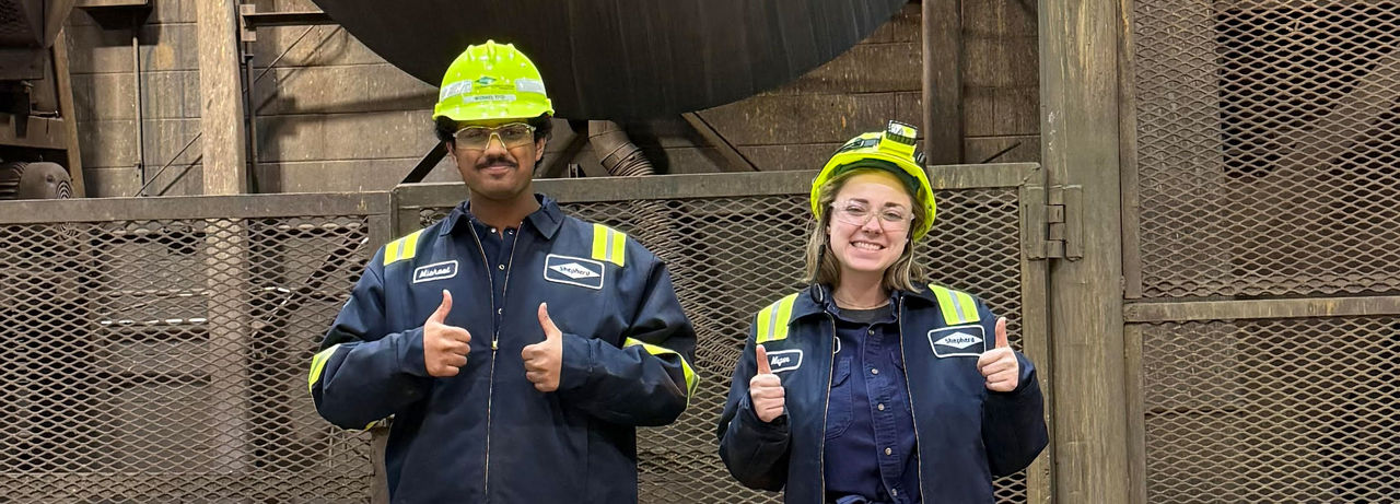 Two Shepherd Color Company employees in safety gear giving a thumbs up in an industrial setting.