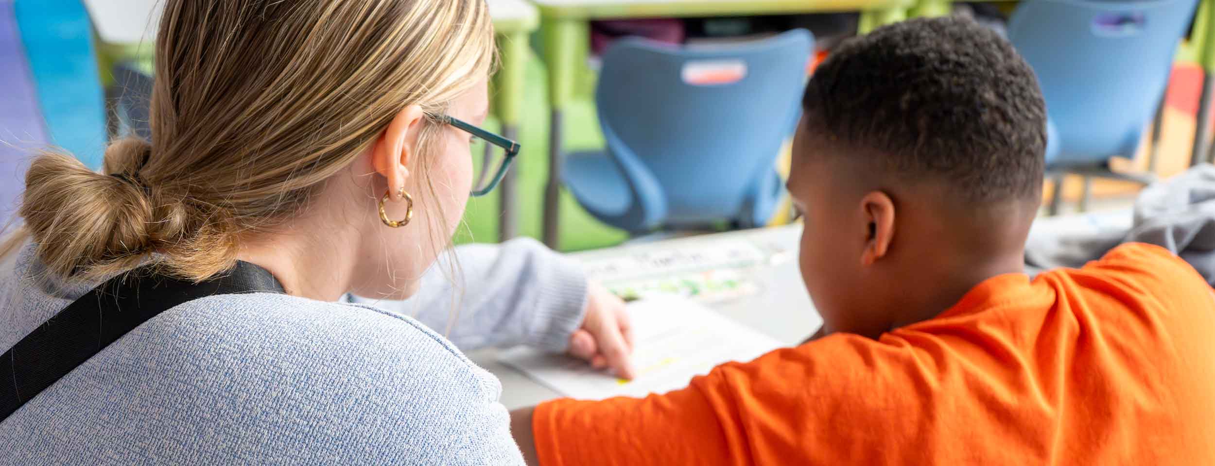 Teaching student sits with young student as he completes a worksheet