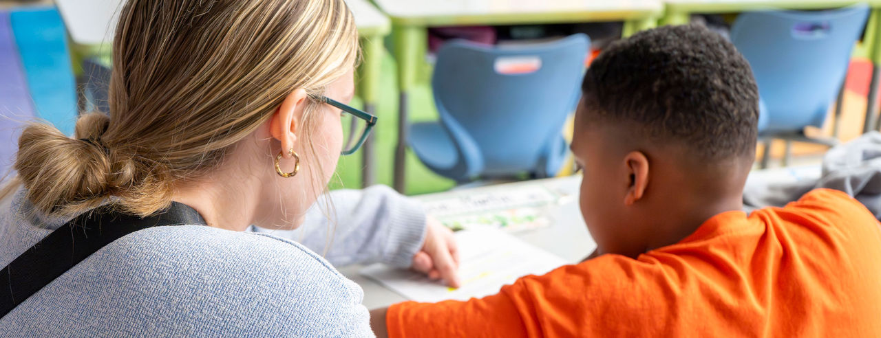 Teaching student sits with young student as he completes a worksheet