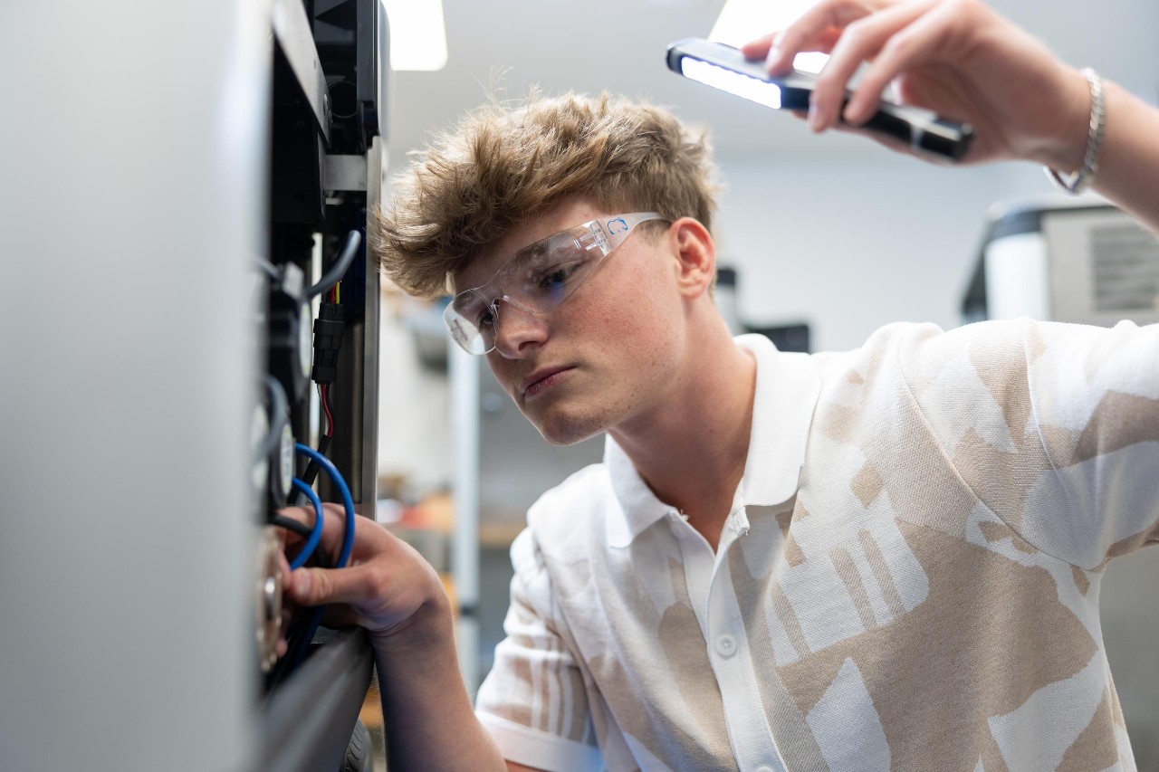 Co-op in college student inspecting machinery with a flashlight as part of his cooperative education experience