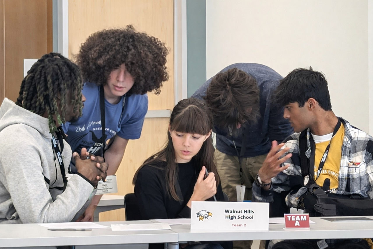 Five high school students from Walnut Hills High are huddled at their station discussing matters at a previous Ethics Bowl competition