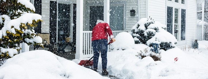 A person shovels snow on a path in front of a house