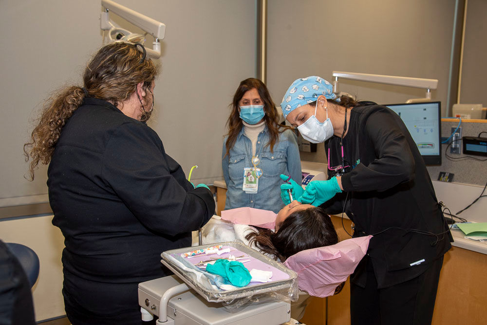 two dental hygiene students and professor working a patient in chair