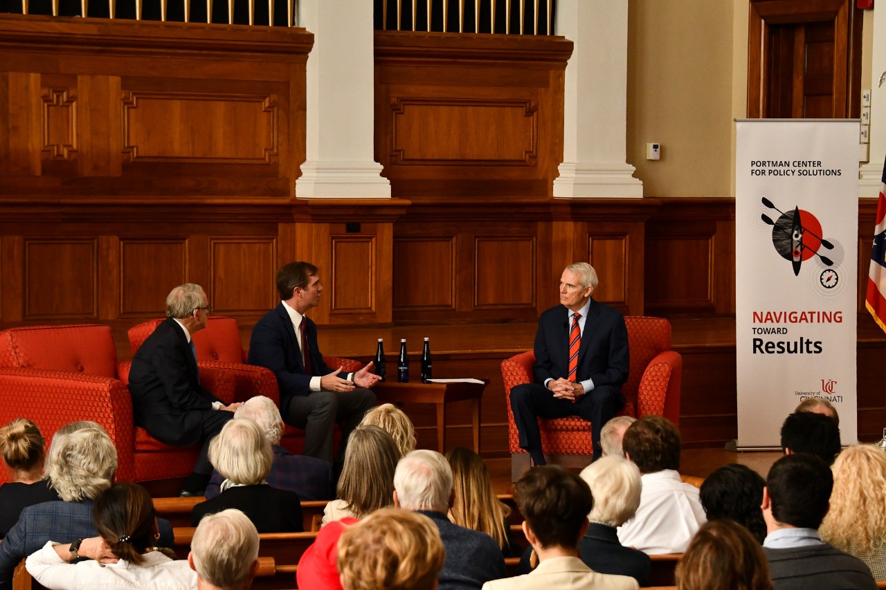 Mike DeWine and Andy Beshear talk on stage to former U.S. Sen. Rob Portman at Probasco Auditorium.