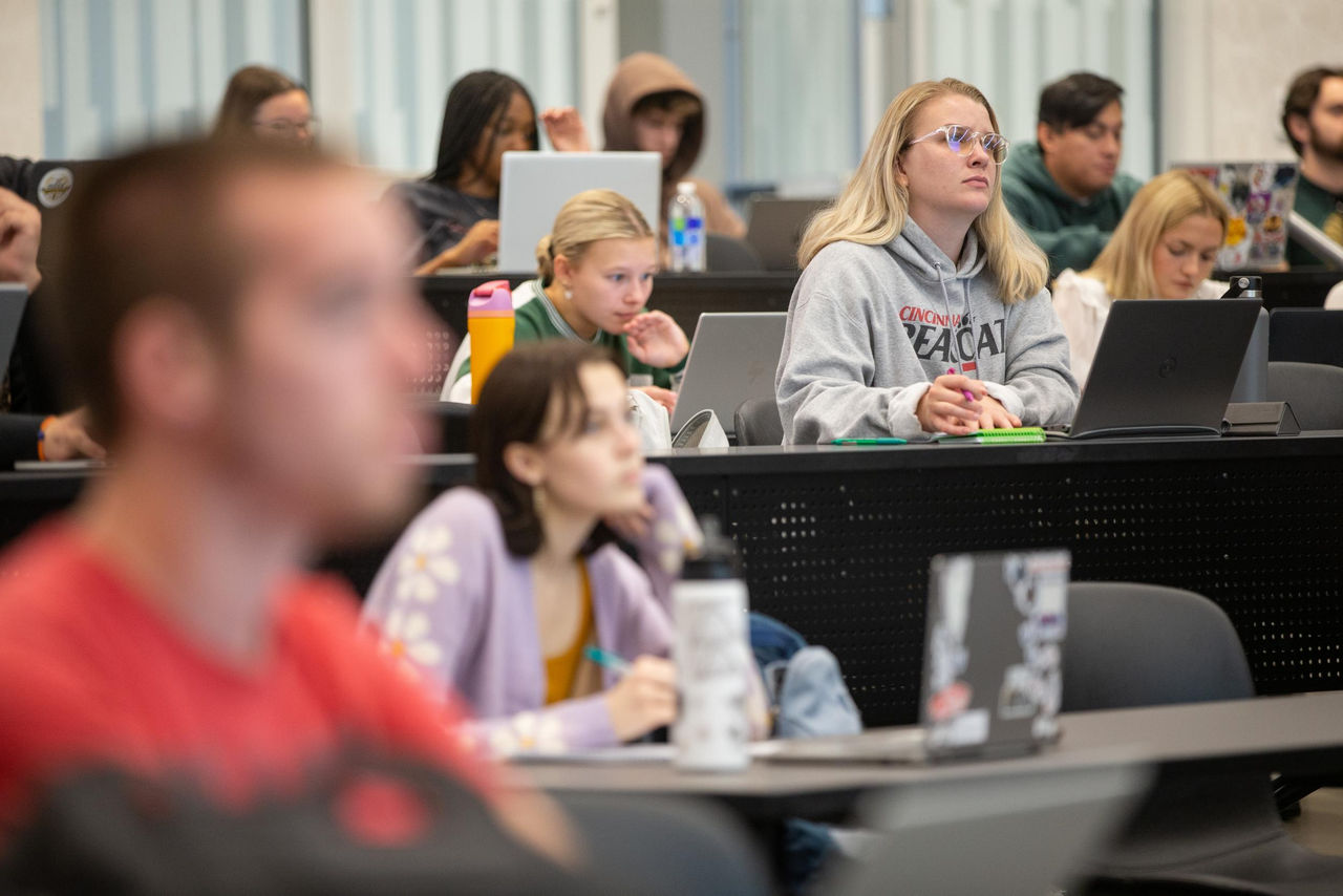 Lecture hall packed with many students seated looking at laptops and listening to a speaker at the University of Cincinnati