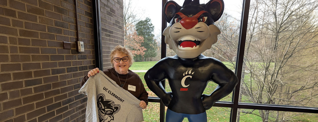Cyndy Wright Sellers holds a UC Clermont shirt and poses with a Bearcat statue on the UC Clermont campus