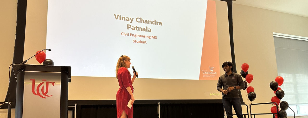 Vinay Chandra Patnala stands on stage with a large screen behind him listing his name. 