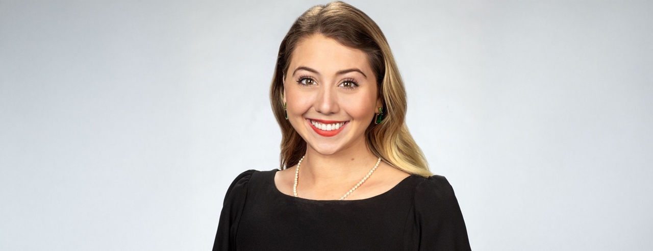 Emma Biros smiles for a headshot. She's wearing a black top and a white pearl necklace.