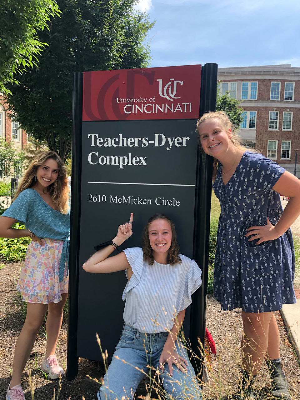 Emma Biros with two unidentified college students stand in front of a sign for Teachers-Dyer Complex at UC