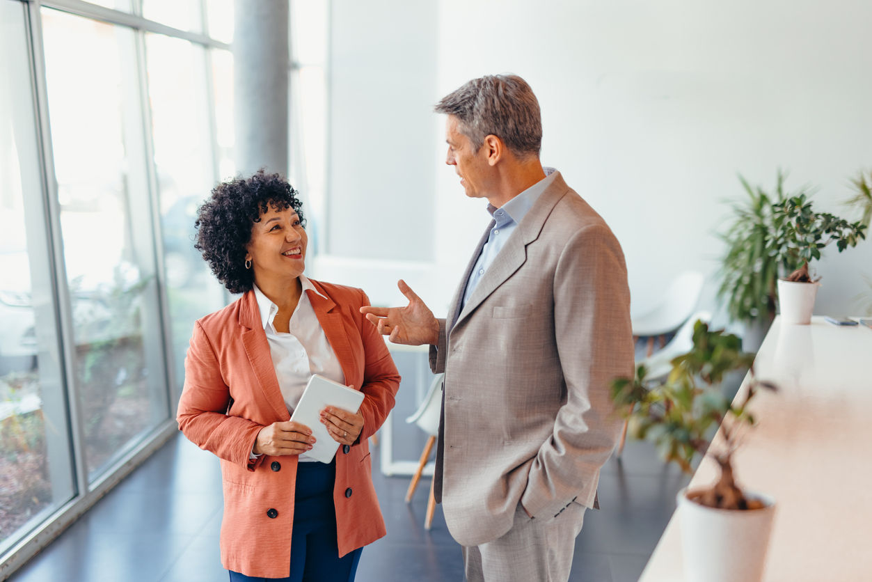 Two colleagues in a modern office setting are engaged in a focused discussion. Both express professionalism and collaboration, highlighting teamwork and effective communication in a corporate environment.