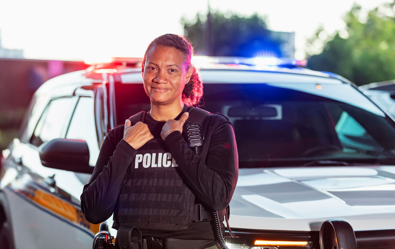 Policewoman stands in front of a police car smiling.