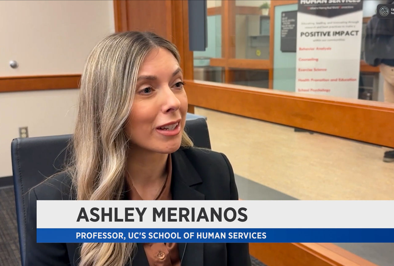 A screenshot of a Spectrum News interview featuring Ashley Merianos and a caption with her name and UC title