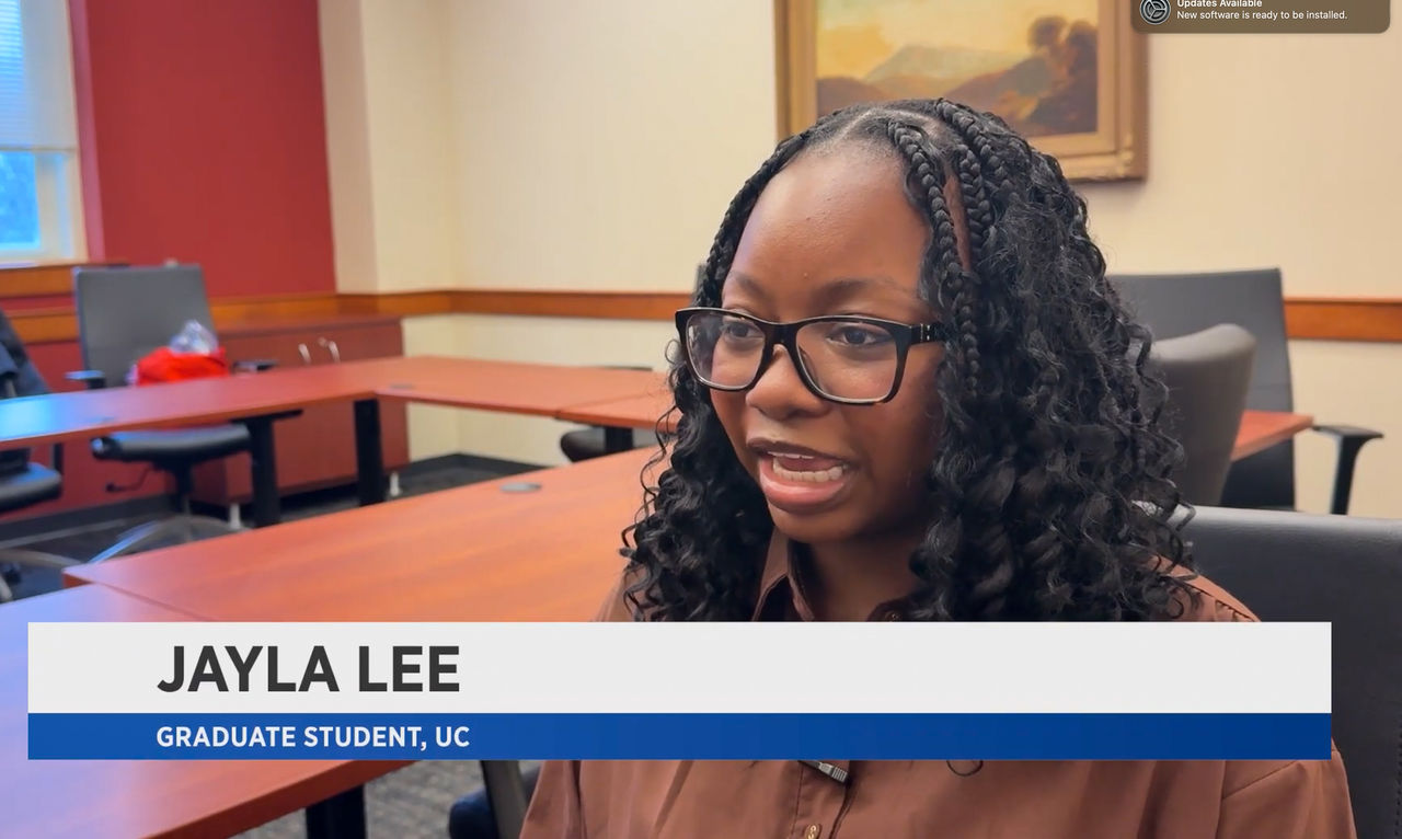 A screenshot of a Spectrum News interview of Jayla Lee with a caption featuring her name and her UC graduate student title.