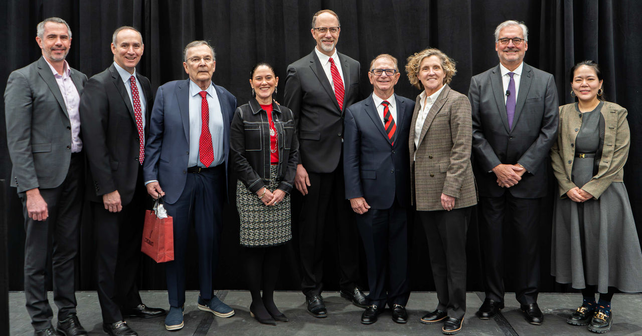 Lindner faculty and staff and real estate professionals pose for a picture, standing on a stage with a black background.
