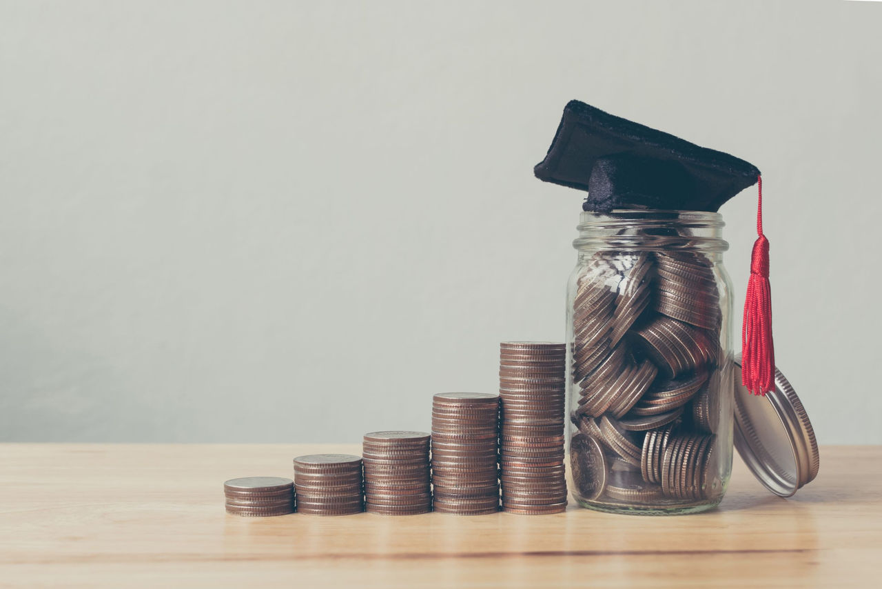 six stacks of coins in the shape of a stairway with a graduation cap on the highest peak