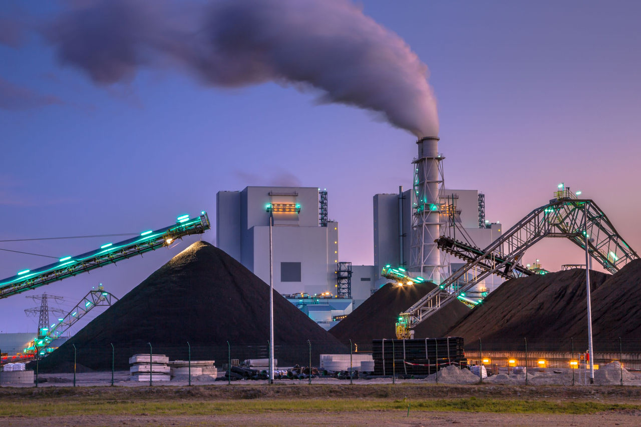Coal plant spewing smoke and big mounds of coal near the operation.