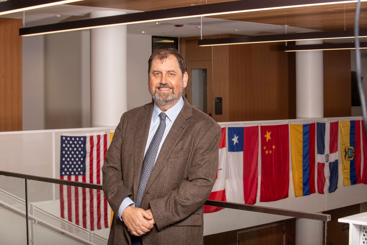 Neil Taylor stands in the atrium of the UC College of Law. In the background are several country flags.