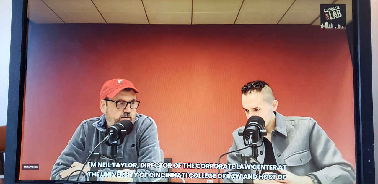 Neil Taylor and Kris Caudell are shown speaking into microphones as they host the Corporate Law Lab Podcast.