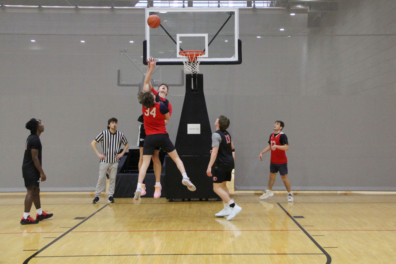 Two students jump in front of a basketball hoop, one attempting to make a basket.