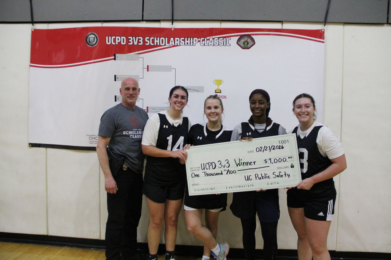 A UCPD officer poses with four students. The students are holding a large check.