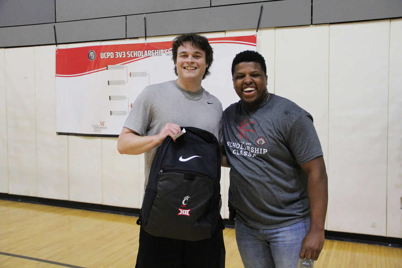Two people pose on a basketball court with a backpack.