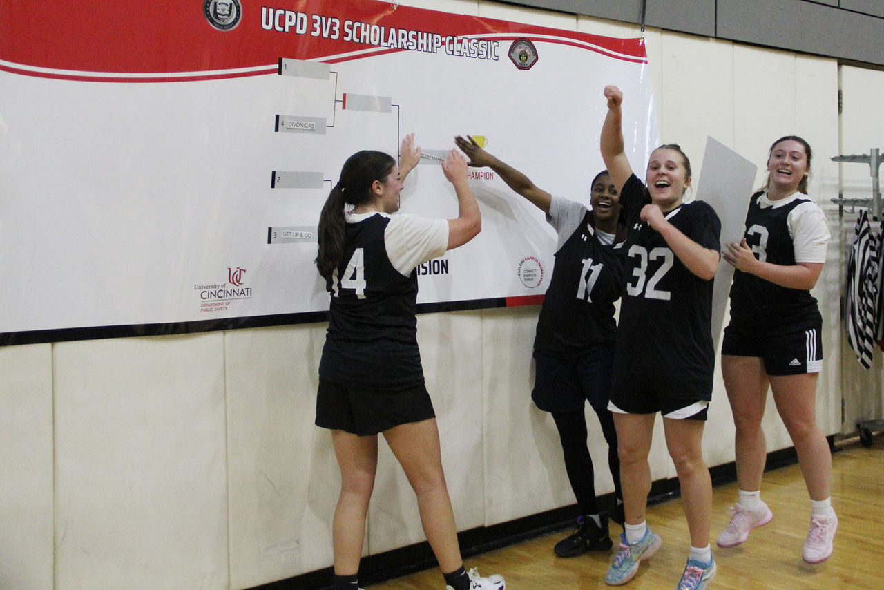 Two students press their team name onto the "champion" spot on a bracket while two other students stand by and cheer.
