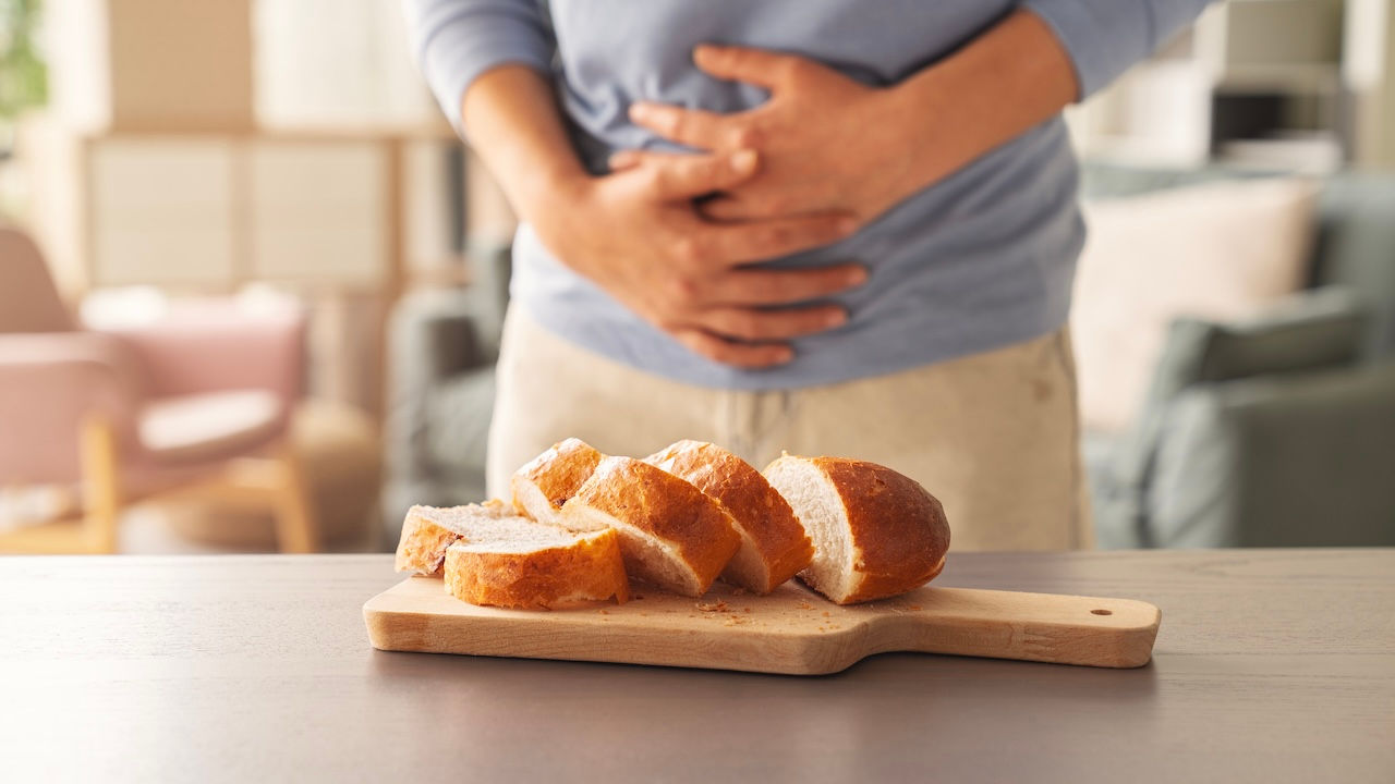 Person holds hands over stomach as sliced bread sits nearby
