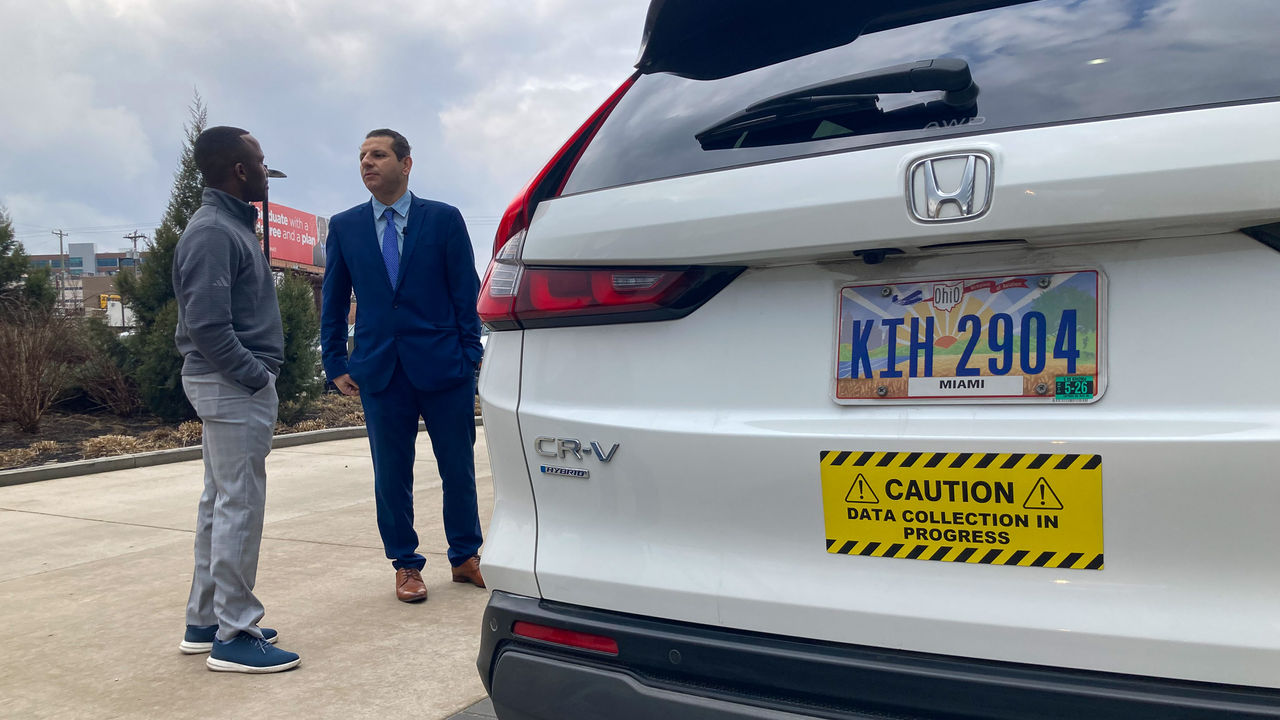 WLWT's Aaron Thomas talks to Munir Nazzal next to a vehicle with the bumper sticker reading caution data collection in progress.
