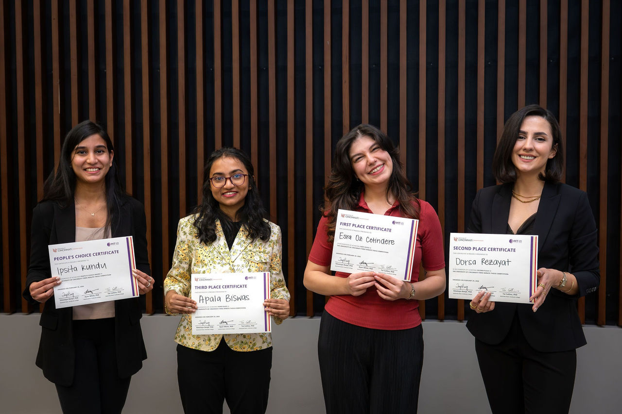 Four women pose with certificates in hand, smiling in front of a wall.