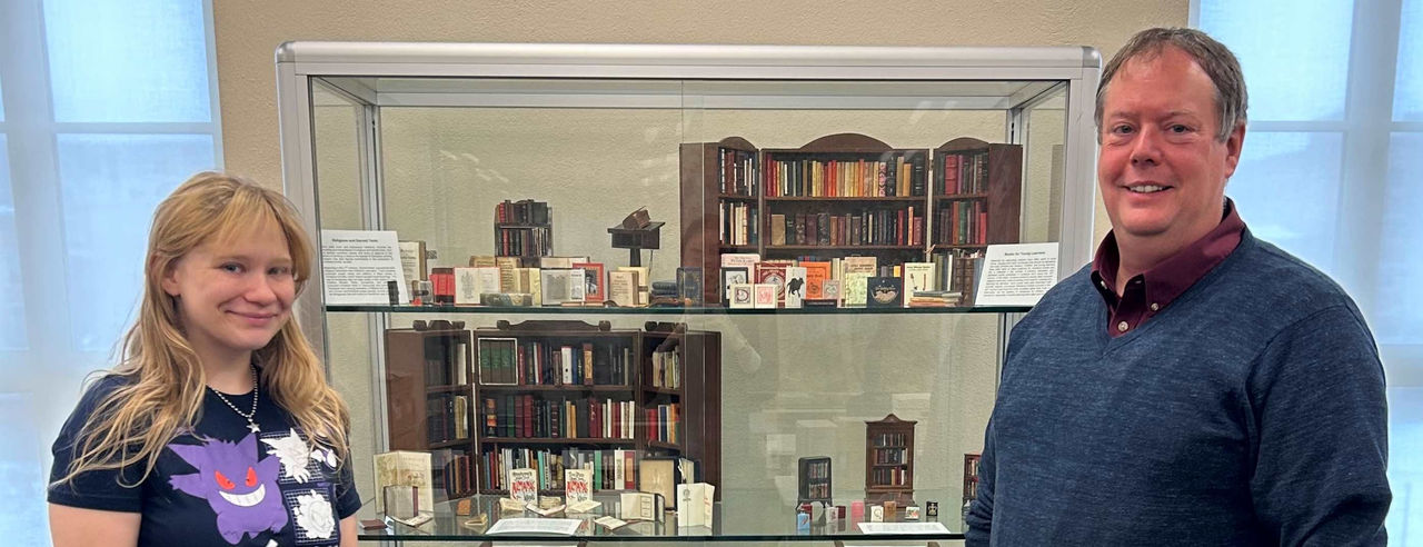 two people in front of a case of mini books