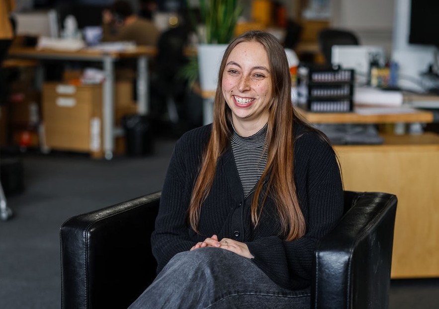 Abby Boyle sits in a chair with desks behind her at Kaleidoscope Innovation.
