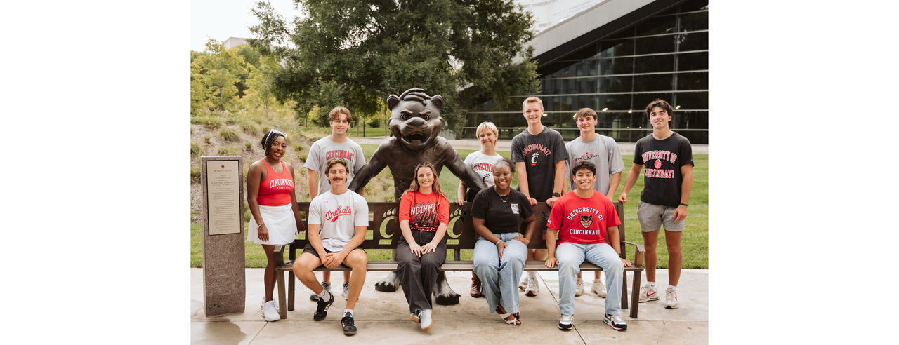 Group of students smiling sitting on the Bearcat bench