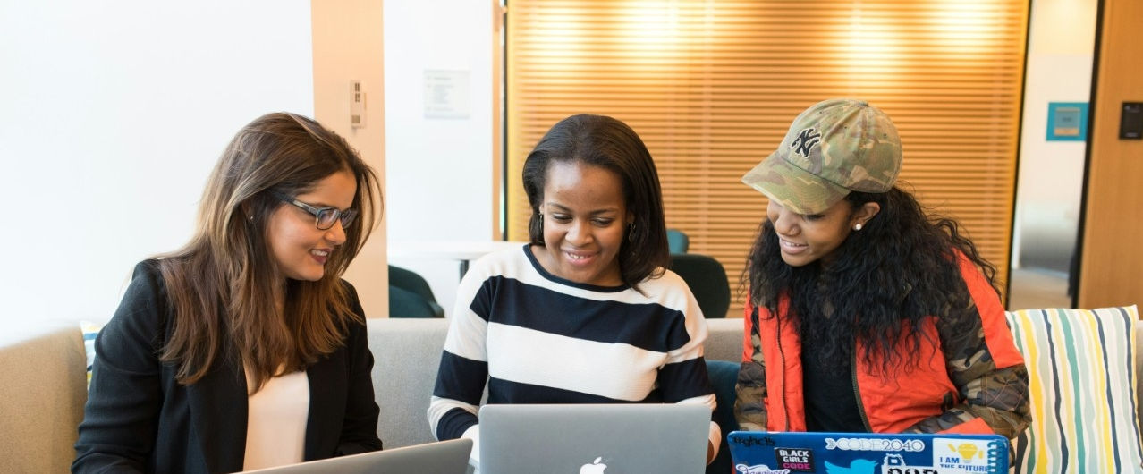 Three women seated at a table, each using a laptop, engaged in discussion and collaboration.