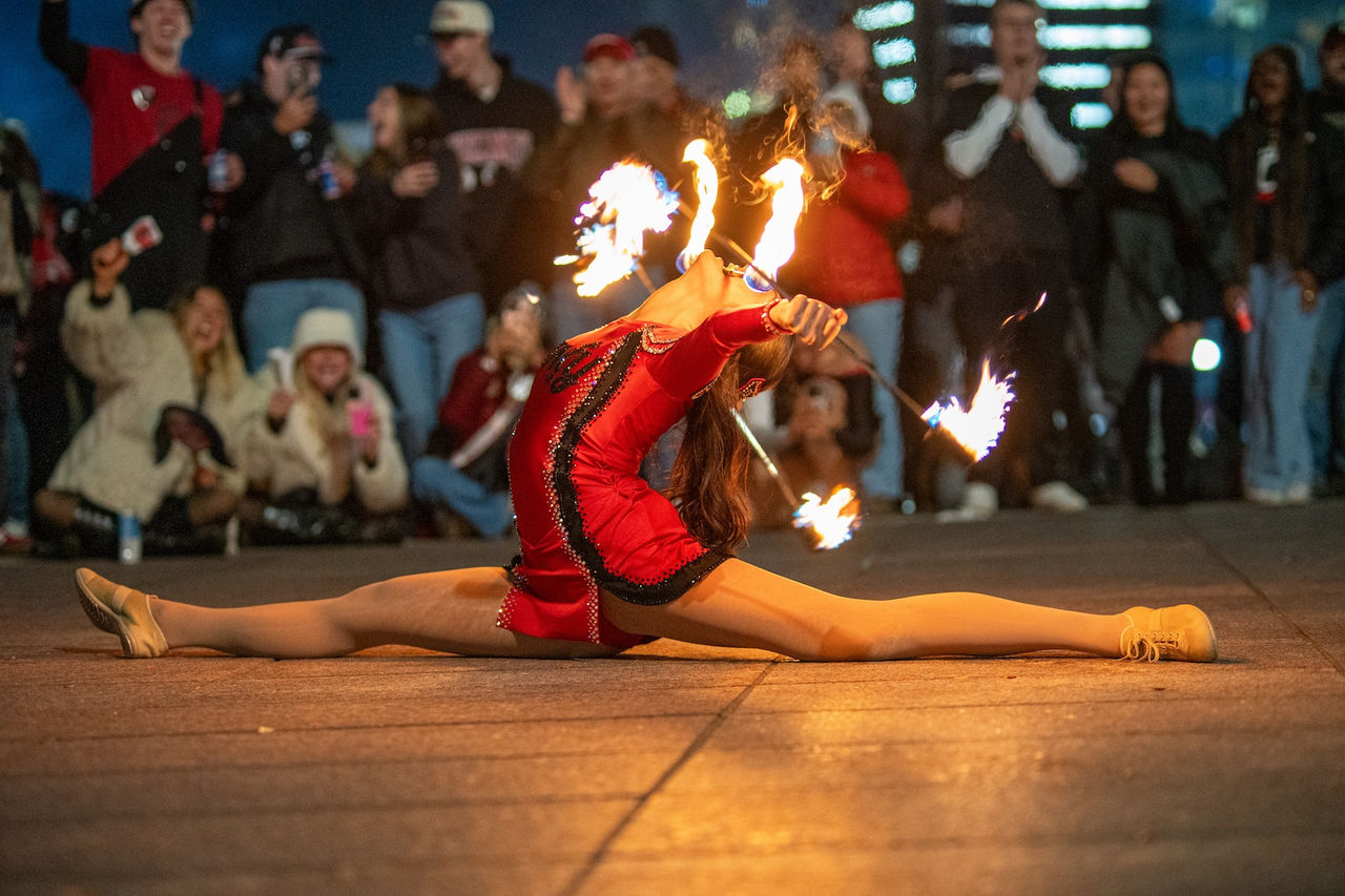 Lexi Peats does the splits while she holds flaming batons in each hand. 