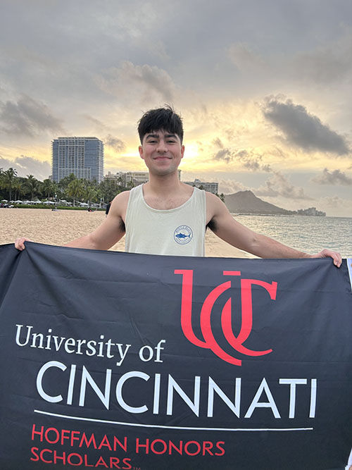 Zane Sawyer on the beach holding a University of Cincinnati Hoffman Honors Scholars flag