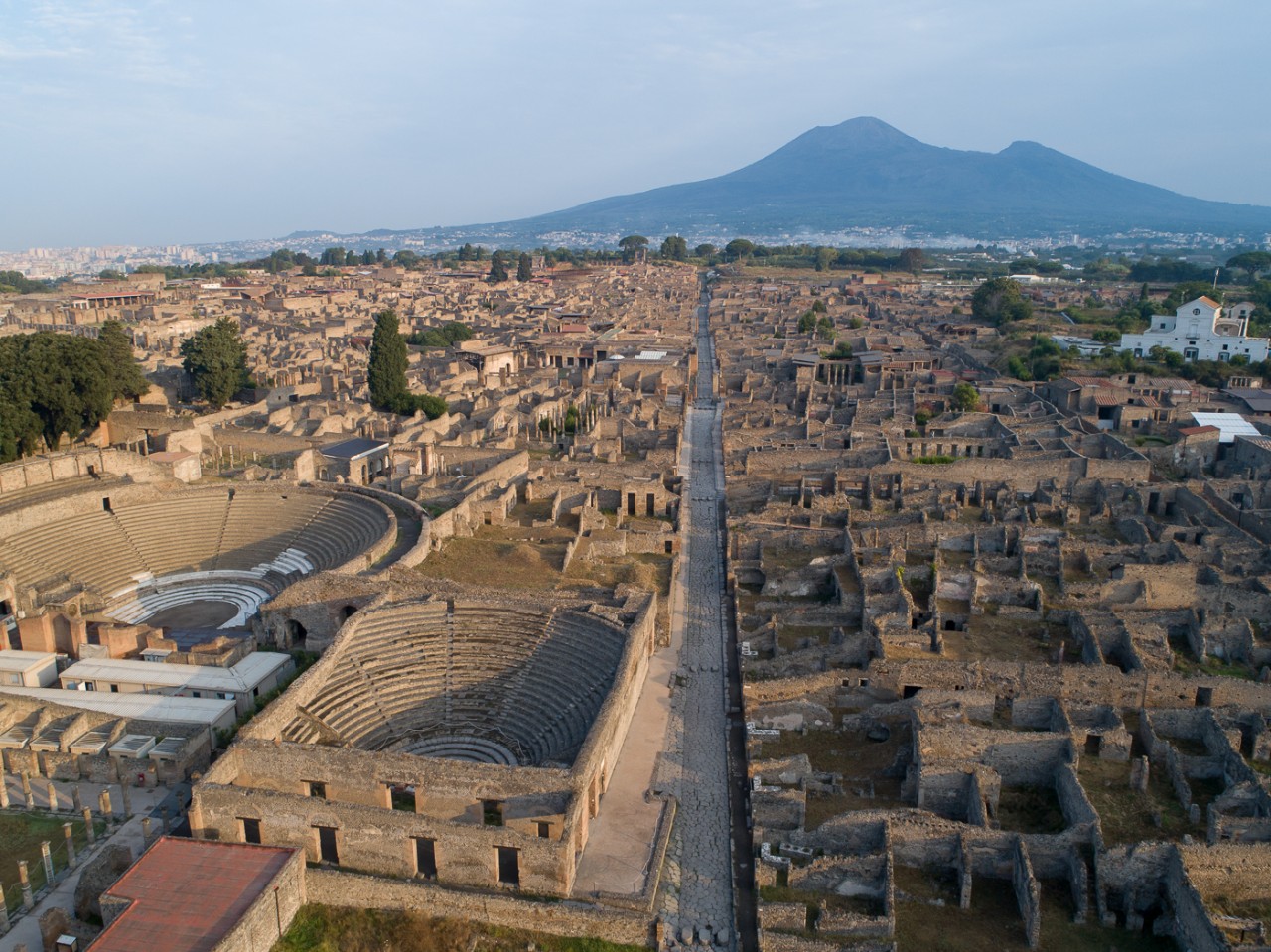 An aerial shot shows the city of Pompeii with Mount Vesuvius in the background.