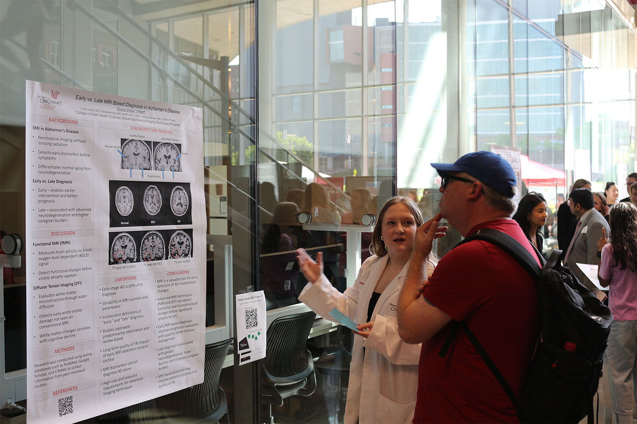 Student presenting research poster to an attendee in the Health Sciences Building atrium