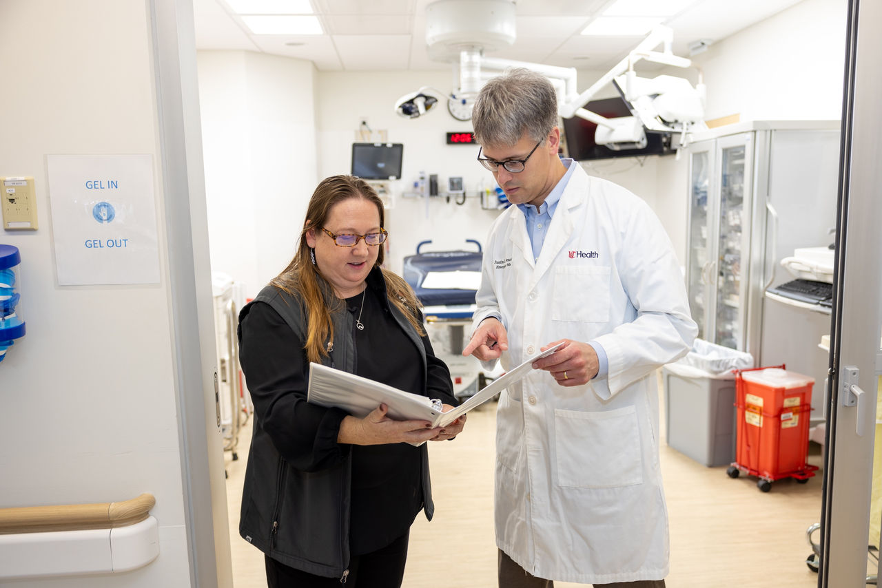 Justin Benoit, MD, talks to a colleague holding a binder in the UC Health emergency medicine clinical trials area 