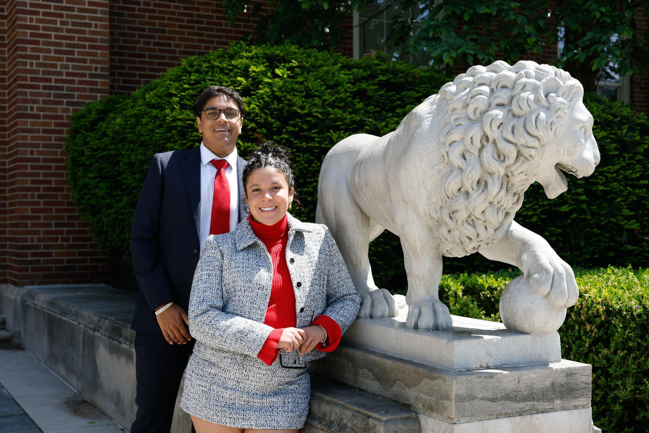 students stand next to a statue of a lion on the UC campus