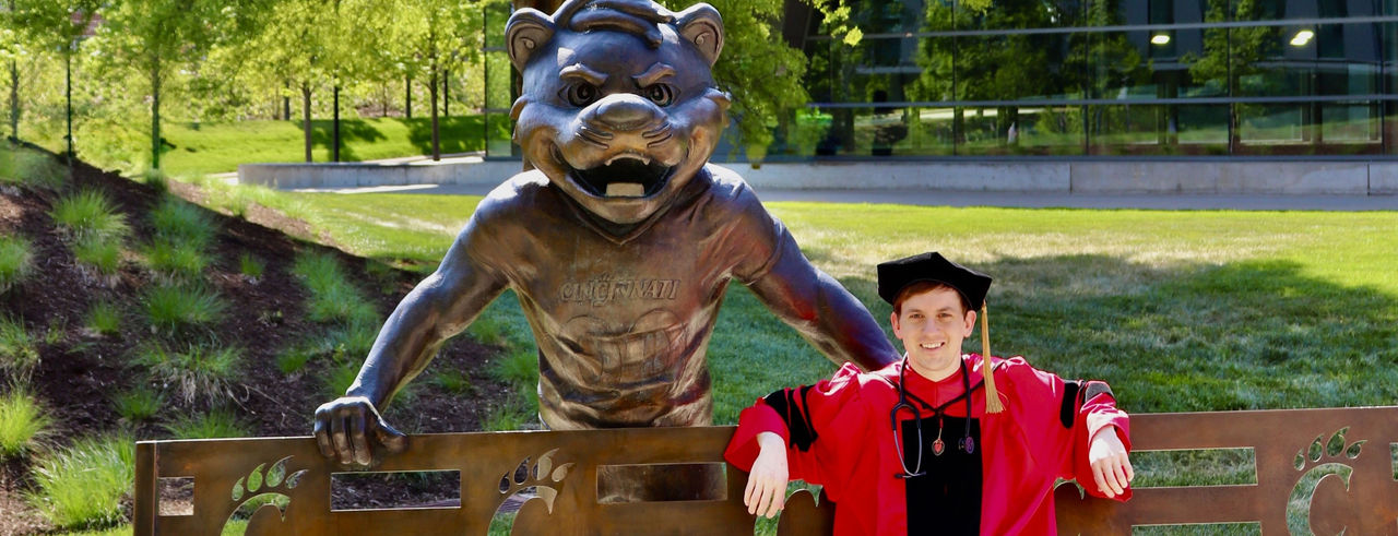 Matt Depenbrock sitting at a bench with Bearcat statue behind him