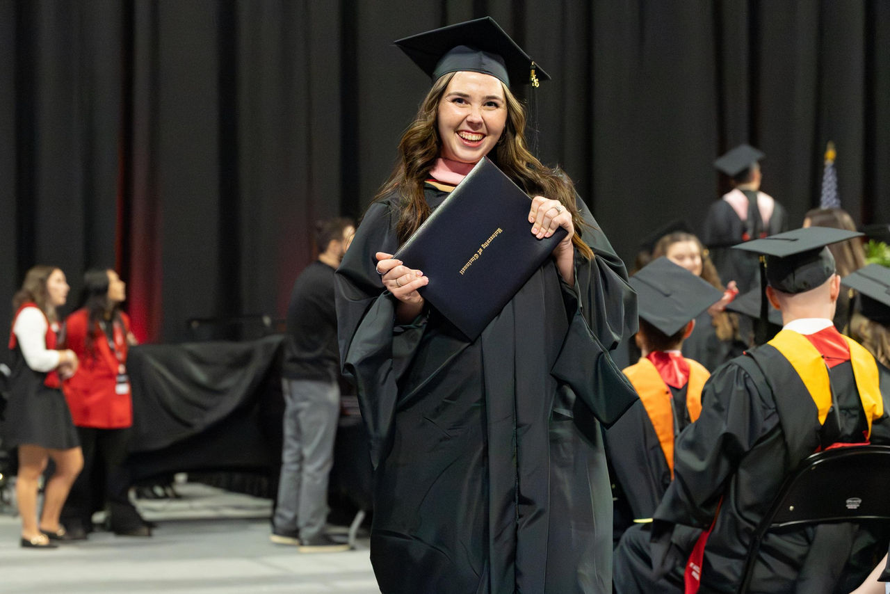 A student in her cap and gown holds up her diploma.