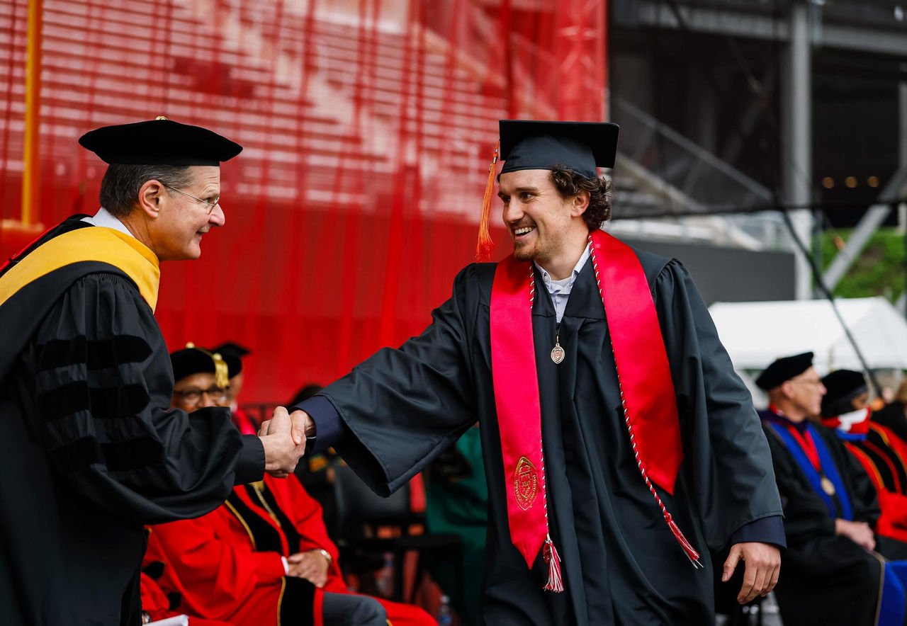 A student in a cap and gown shakes hands with a faculty member on stage.