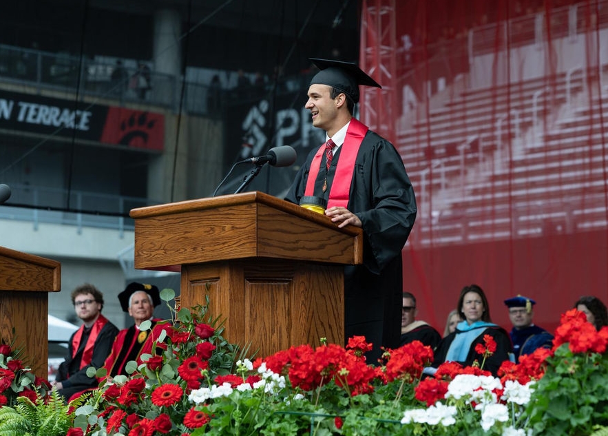 Seth Engelhardt in a cap and gown stands at a podium on stage.