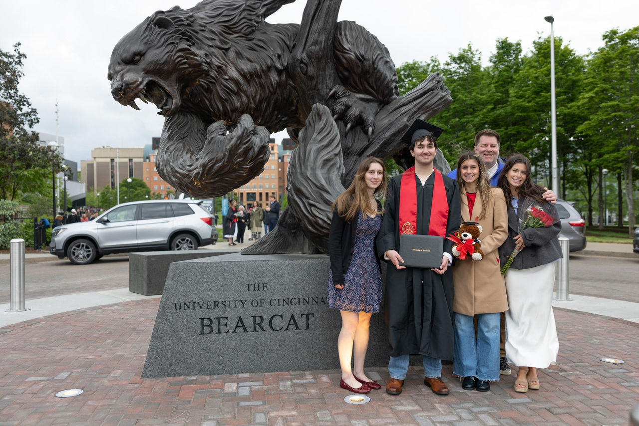 A student takes a family photo in front of the Bearcat statue.