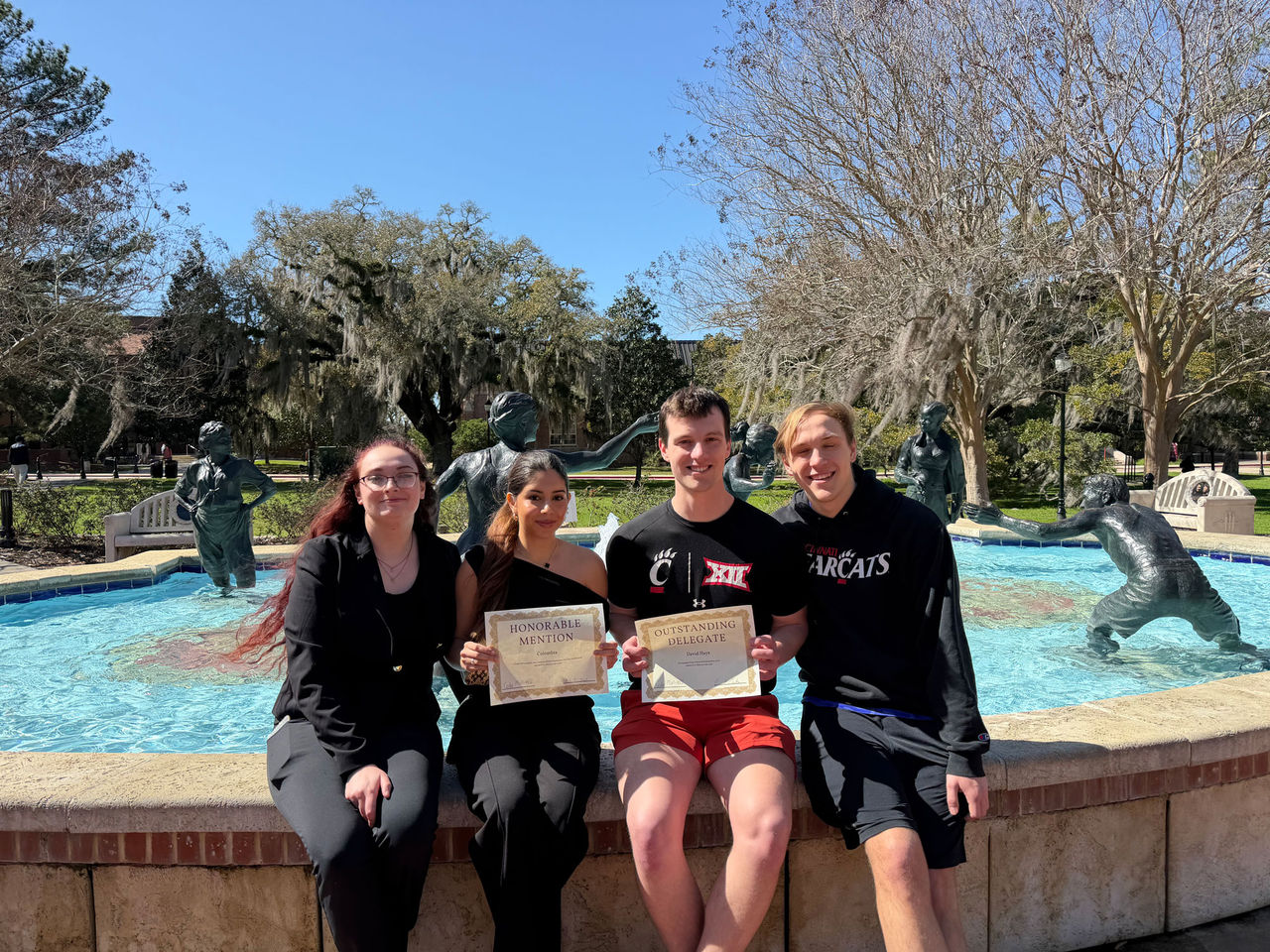 Students sitting on the lip of a fountain showing off their awards