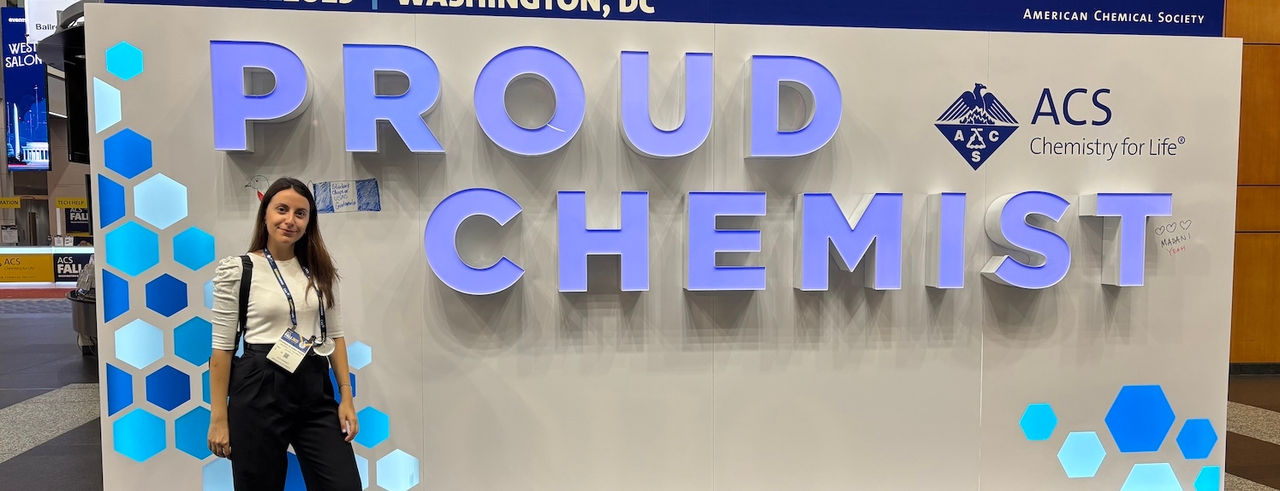 Evangelia Anna Passa at a conference in front of an LED sign that reads "Proud Chemist" 