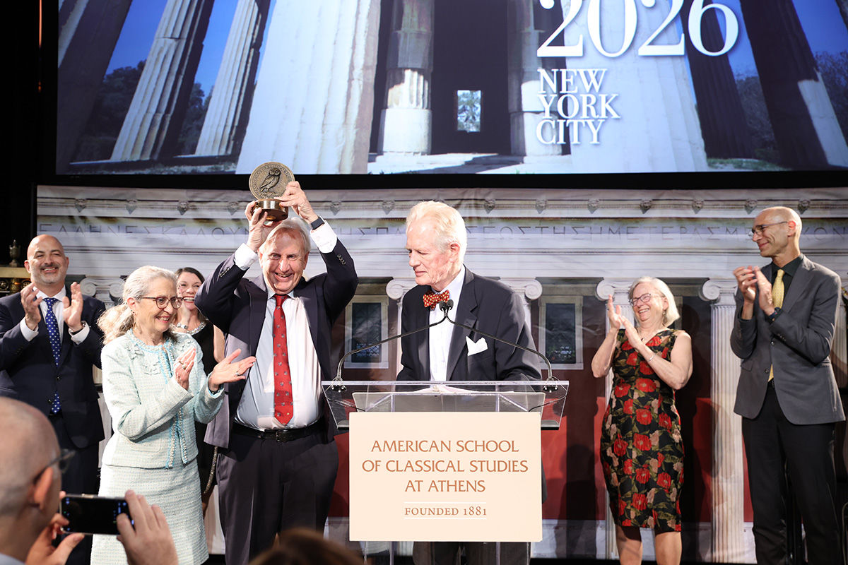 Jack Davis standing next to Sharon Stocker holds up his Rome Prize on stage surrounded by supporters.