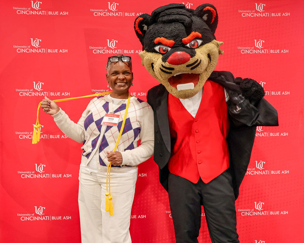 woman posing with bearcat mascot in front of red UC Blue Ash College backdrop